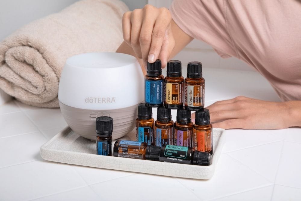 a lady arranges many oil bottles next to a diffuser