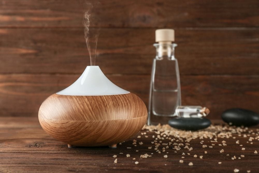 A electric diffuser, essential oil bottles, rocks and salts on a woody table
